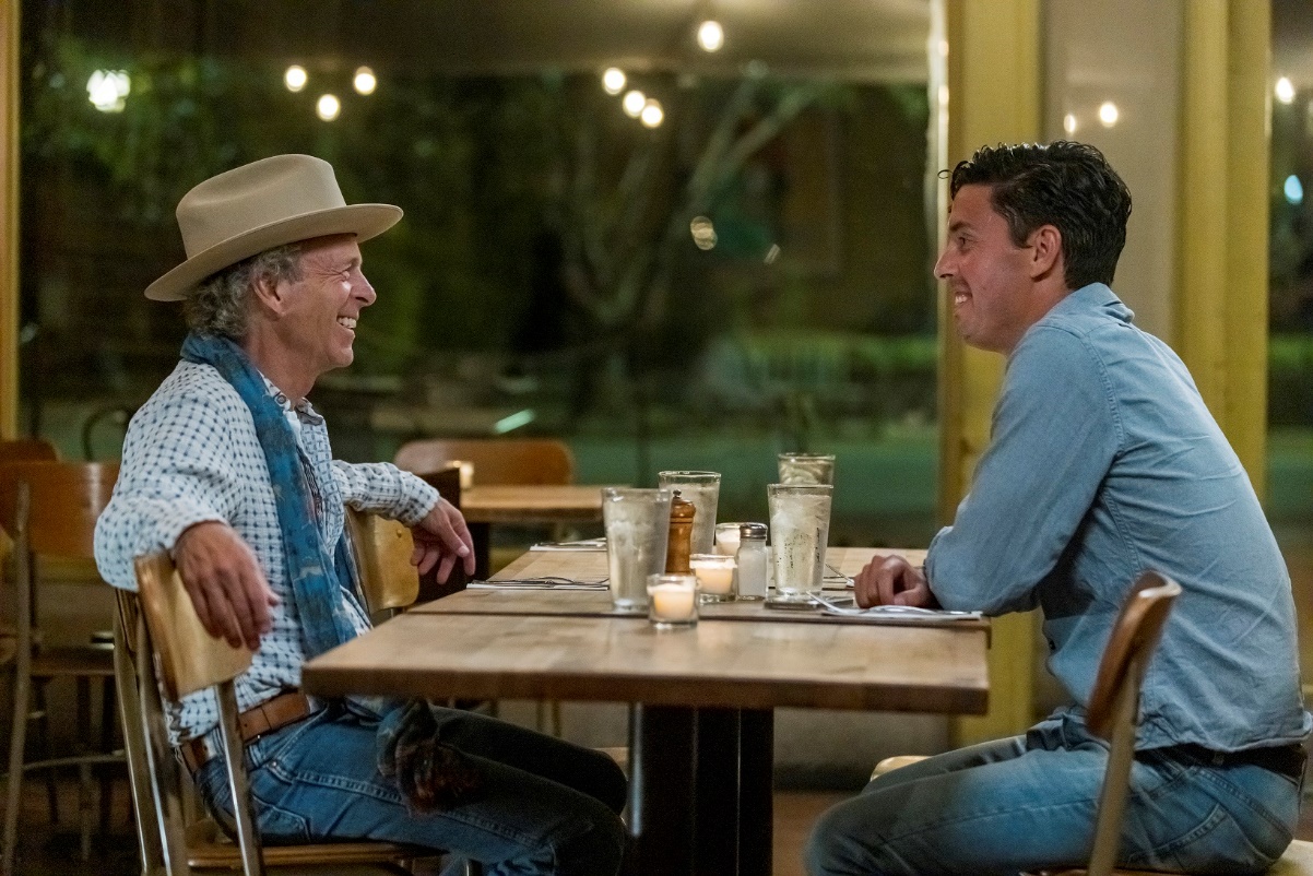 A couple of men sitting at a table with drinksDescription automatically generated with medium confidence