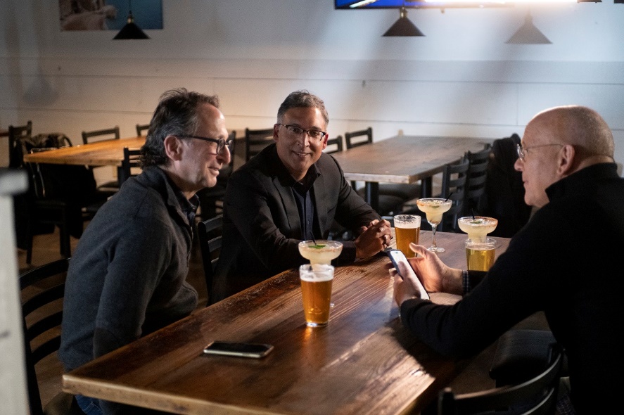 A group of men sitting at a table with drinksDescription automatically generated with medium confidence