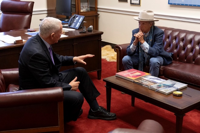 A person in a suit and hat talking to another personDescription automatically generated