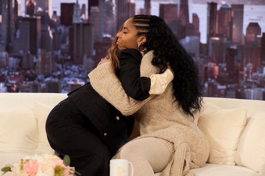 Two women hugging on a couchAI-generated content may be incorrect.